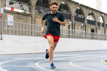 Young runner man wearing sports clothes running in track and field.