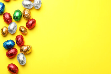 Chocolate eggs wrapped in colorful foil on yellow background, flat lay. Space for text