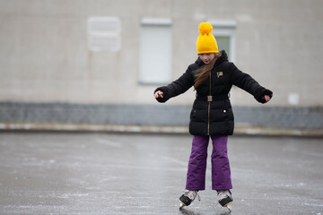 A little girl in a yellow hat is skating.