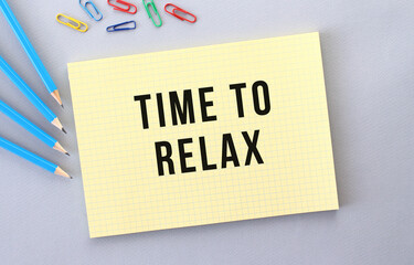 TIME TO RELAX text in notebook on gray background next to pencils and paper clips.