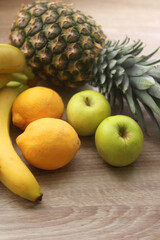 Pineapple, bananas, apples an dlemons on wooden background. Selective focus.