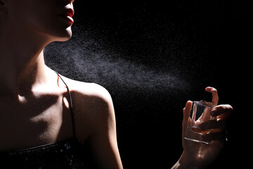 Woman spraying luxury perfume on black background, closeup