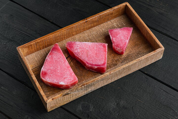 Obraz na płótnie Canvas Frozen tuna fish steaks, in wooden box, on black wooden background