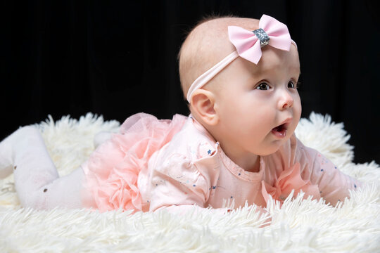 Beautiful baby girl in pink clothes on a black background. Baby at four months old. A funny child.