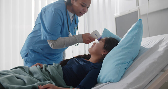 Doctor measuring temperature of asian child patient with infrared thermometer in hospital ward