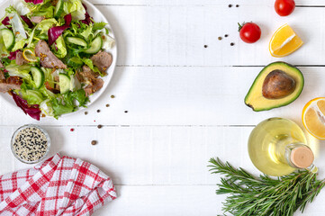 Ingredients for cooking with copy space. Bowl of fresh salad, rosemary, lemon, spices and oil on white wooden table. Food background. Healthy eating concept.
