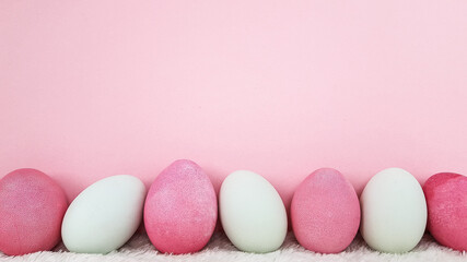 pink and white eggs stand in a row on a light pink background. there is also room for text. postcard for congratulations on the day of bright Easter.