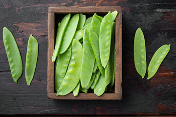 Sugar snap peas, raw ripe baby pods, in wooden box, on old dark  wooden table background, top view flat lay