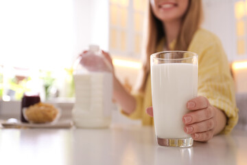 Young woman with gallon bottle of milk, glass and breakfast cereal at white table in kitchen, closeup