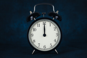 Black vintage alarm clock shows 12 o'clock isolated on dark background. Wake up and hurry up