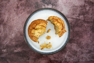 Overhead view of a single cinnamon crumb muffin broken in pieces on a plate atop a maroon tabletop.