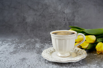 cup of black coffee on stone surface and bouquet of yellow tulips