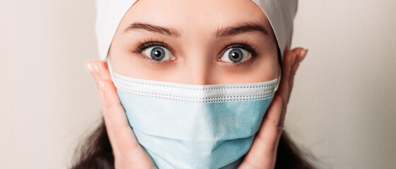 Shocked excited amazed nurse young medic standing and looking at the camera. Female doctor dressed in medical gown and surgical hat. Pandemic virus coronavirus concept, disposable face mask copy space