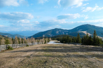 A panoramic view on an Alpine chain in Austria, partially covered with snow. The vast pasture has golden color. There is Rappoldkogel in the back. A vast ski slope in spring. Blue sky and white clouds
