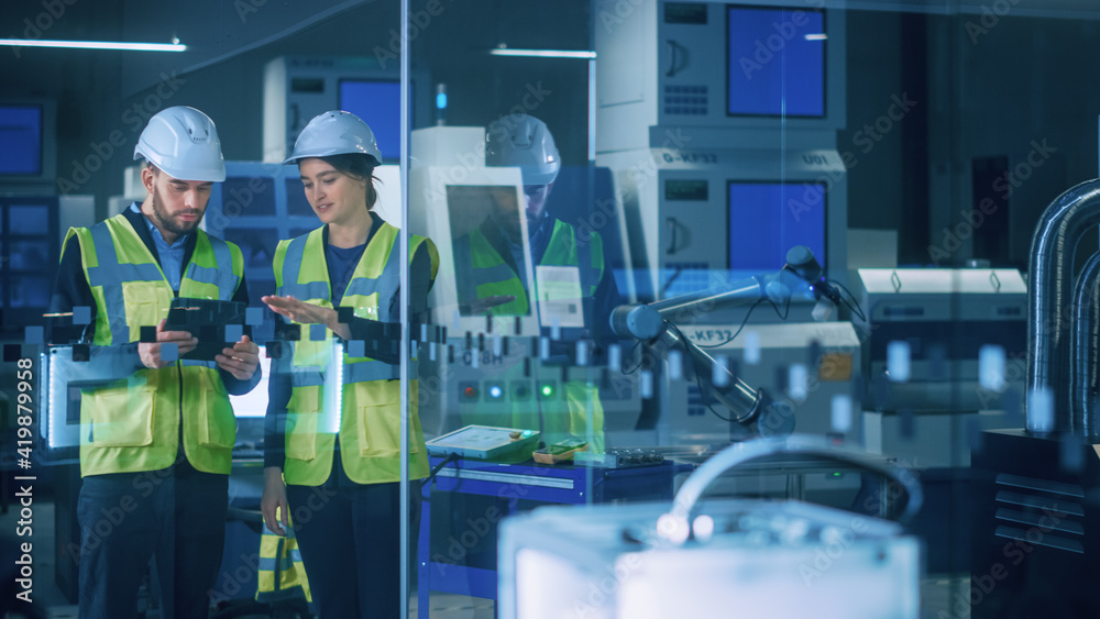 Poster modern factory: female and male engineers wearing safety jackets, hardhats standing in industrial wo