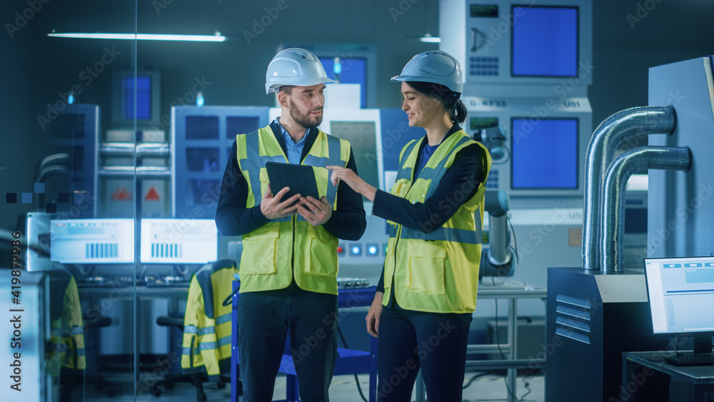 Poster modern factory: female and male engineers wearing safety jackets, hardhats standing in industrial wo