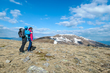 A coupe holding hands while hiking to the top of Ameringkogel in Austrian Alps. There is still some snow on the slopes. The vast pasture is golden. There are other chains in the back. Happiness