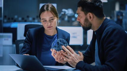 Industry 4.0 Modern Factory Meeting Room: Chief Engineer Holds Mechanism, Shows it to Female Designer, They Talk. Scientists in Contemporary Lab Build Electronic Machinery for With Futuristic Design