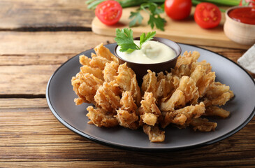 Fried blooming onion with dipping sauce served on wooden table