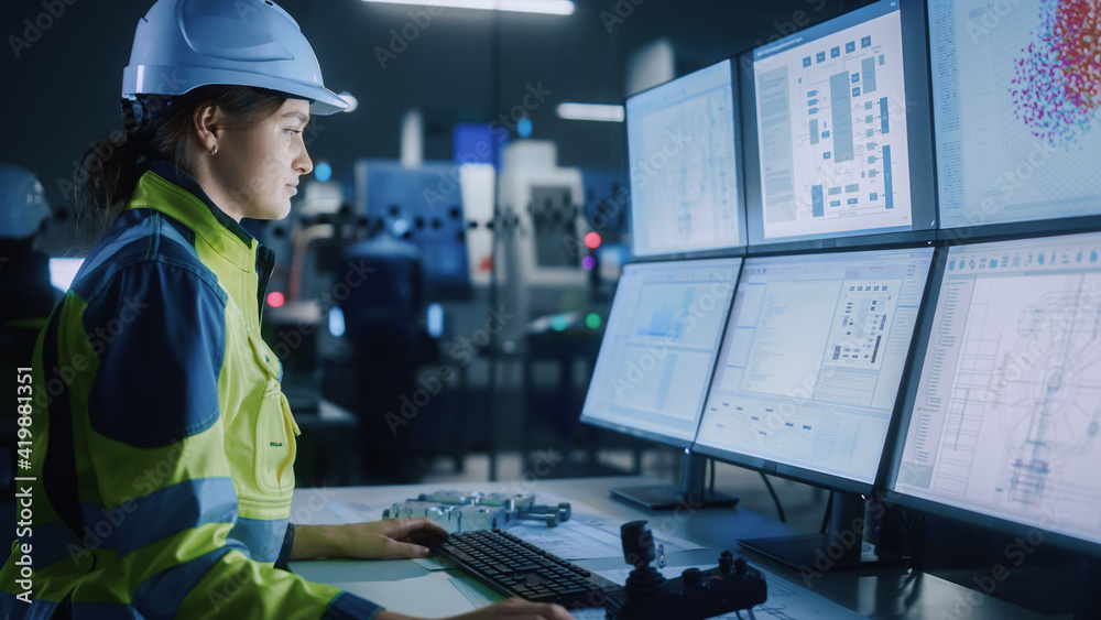 Wall mural Industry 4.0 Modern Factory: Female Facility Operator Controls Workshop Production Line, Uses Computer with Screens Showing Complex UI of Machine Operation Processes, Controllers, Machinery Blueprints