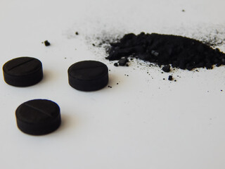 activated charcoal in tablets and in bulk on a white background