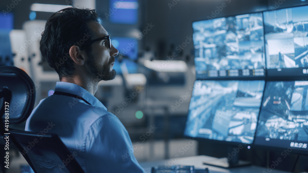 Poster Industry 4.0 Modern Factory: Portrait Shot of a Security Operator Controls Proper Functioning of Workshop Production Line, Uses Computer with Screens Showing Surveillance Feed. High-Tech Security