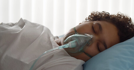 Oxygen mask on afro woman patient lying in bed