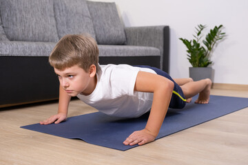 Boy on yoga mat at home holding plank pose. Child physical activity on quarantine Healhty lifestyle...