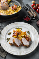 Roasted pork loin with mash potatoe gratin, sage and prosciutto, on plate dish, on gray stone background