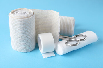 Medical bandage rolls, sticking plaster and scissors on light blue background