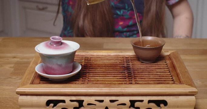 Cropped close up shot of tea master pouring tea water in bowl. Front view of man brewing hot oolong drink on wooden table chaban at kitchen. Oriental Chinese ceremony preparing concept