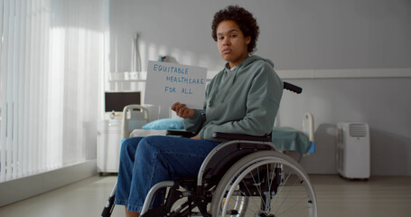 Upset afro patient in wheelchair at hospital ward and holding equitable health care for all poster