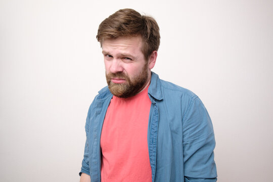 Caucasian bearded man distrustfully and contemptuously looks into the camera. White background.