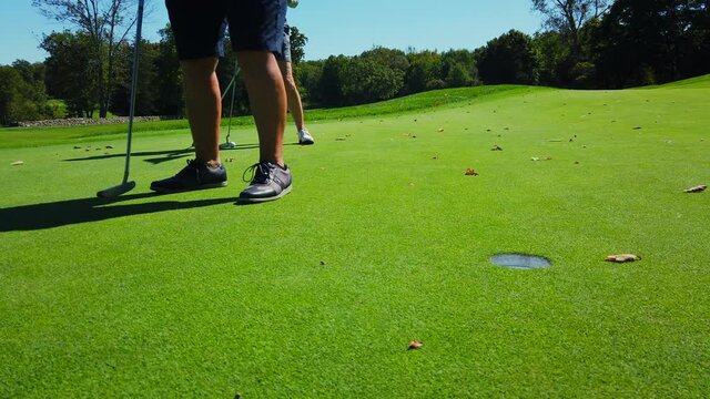 Close up on green as golfer sinks a short putt into the cup