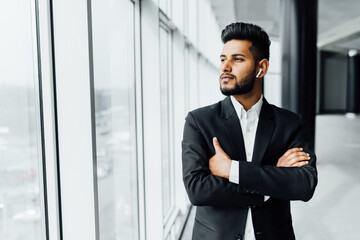 Fototapeta premium Indian man with a beard, solid appearance, he stands by the window in a modern building
