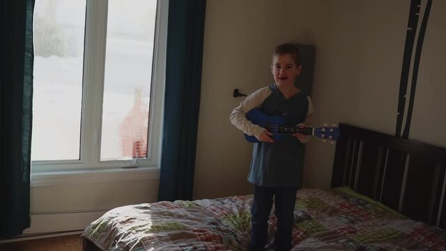 Cheerful Caucasian boy playing guitar on his bedroom