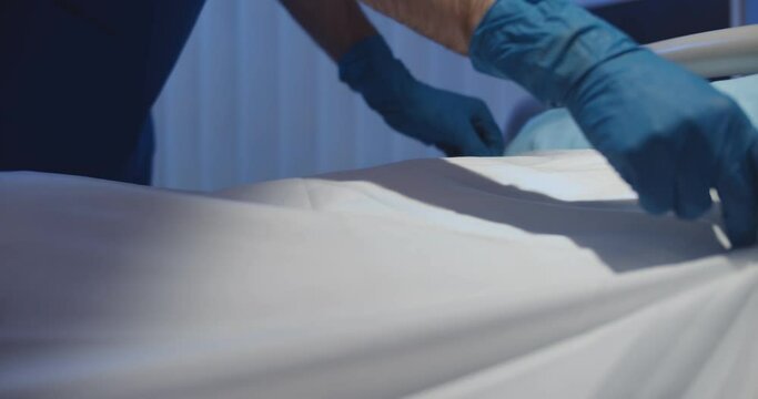 Close up of doctor in protective gloves covering dead young african female patient with sheet