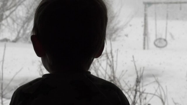 Silhouette of small child admiring beautiful snowfall through window