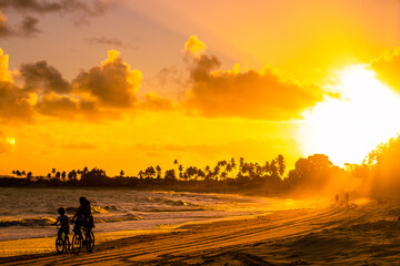 Fototapeta na wymiar Mãe e filho passeiam de bicicleta durante o pôr do sol na praia.