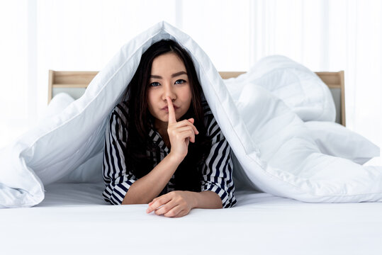 Portrait images of Asian attractive young woman under the blanket, Use the fingers to make a symbol do not make a noise and the secret, to people concept.