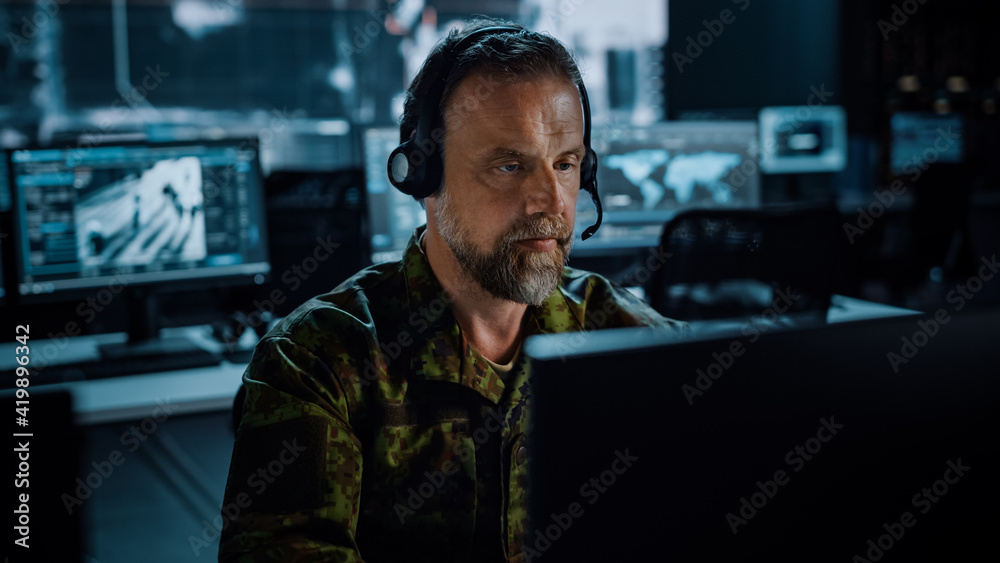 Poster bearded military surveillance officer in headset working in a central office hub for cyber operation