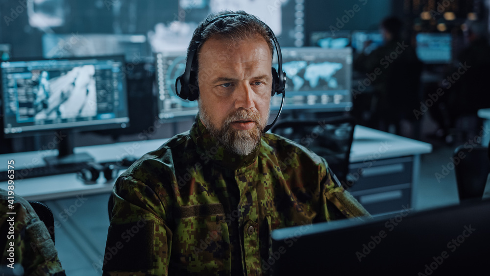 Poster bearded military surveillance officer in headset working in a central office hub for cyber operation