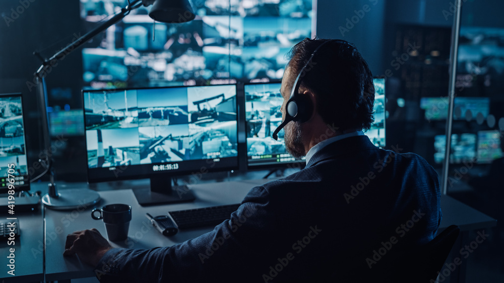Poster Male Officer Works on a Computer with Surveillance CCTV Video in a Harbour Monitoring Center with Multiple Cameras on a Big Digital Screen. Employees Sit in Front of Displays with Big Data.