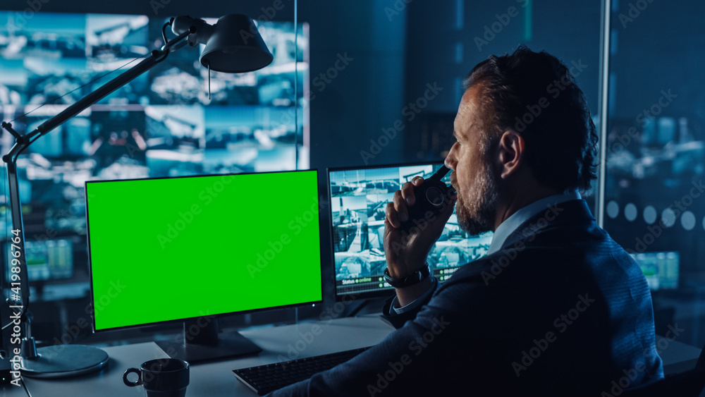 Poster Male Officer Works on a Computer with Green Screen Mock Up in Surveillance Center in a Harbour Monitoring Center with Multiple Cameras on a Big Digital Screen. Employees Sit in Front of Displays.
