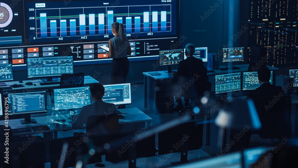 Poster Software Engineers Working in a Room with a Big Screen in a Modern Monitoring Office with Live Analysis Feed with Charts. Monitoring Room Big Data Scientists and Managers Sit in Front of Computers.