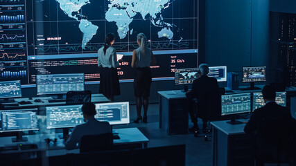 Two Software Engineers Talking Next to a Big Screen in a Modern Monitoring Office with Live...