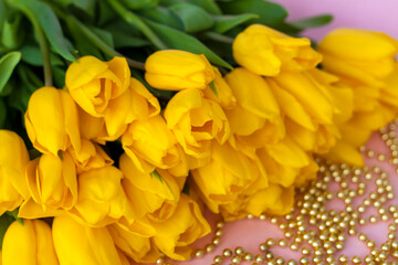 A bouquet of fresh yellow tulips. A bouquet of tulips on a pink background with a scattering of gold beads. Spring flowers in the interior. The concept of spring or holiday, March 8, 