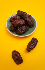 Dates fruit in ceramic plate on color paper background with empty space for your text or message. healthy food concept.