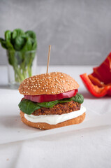 Vegan burger made with red beans, red pepper, spinach, white yoghurt and fresh salad leaves an cut vegetables at the background.