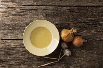 Bowl with clear rich broth. White crockery on an aged wooden table. Vegetables - onions, garlic, spices